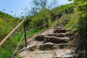 Eine Treppe aus grob behauenen Steinen f&uuml;hrt mit einem Gel&auml;nder bergauf.