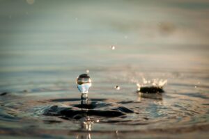 Auf einer ruhigen Wasseroberfl&auml;che springt ein dynamischer Wassertropfen in die H&ouml;he.