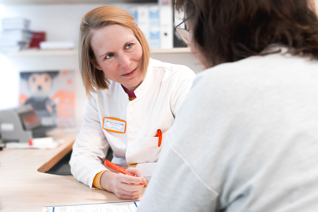 &Auml;rztin im wei&szlig;en Kittel im Gespr&auml;ch mit einer Patientin an einem Schreibtisch im Brustzentrum